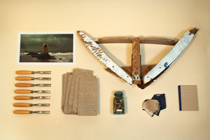 Image of A Kiss for Luck artifacts including: carving knives, photograph, lunch bags, jar of wooden shavings, protective gloves, a journal, and a fragment of the boat bow
