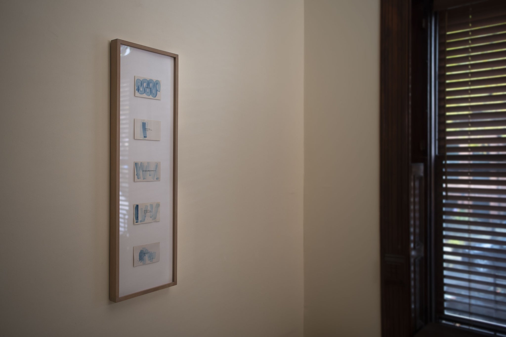 James Leonard - light from a window hitting a framed curation of 5 small, blue watercolor paintings