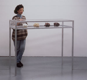 James Leonard - Image of a woman admiring the artwork, Lunar Phases, in a gallery; she examines four realistic hearts made from various materials, which are encased in glass at chest height