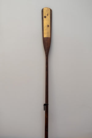James Leonard - Full image of Untitled Oar no. 7, showing gilded center paddle that has been shot through with bullets; metal hardware is present at the stem