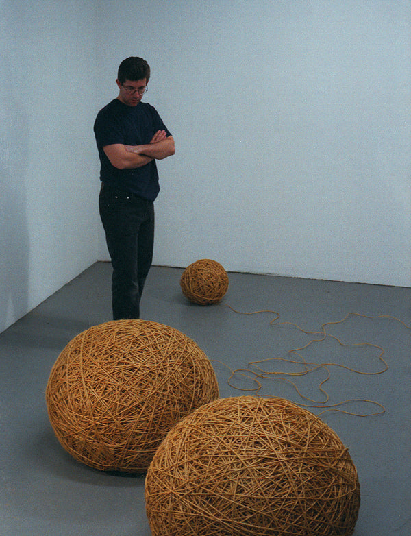 James Leonard - A man in black T-shirt and jeans looks down at the gallery installation, Valentine, comprised of ten miles worth of twine, formed into balls of various sizes