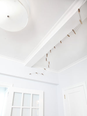 James Leonard - A miniature handmade fence, no. 6 in the Running Fence series, as it travels along a white walled ceiling; entryway light is depicted for scale