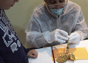 James Leonard - A young boy observes Hector Canonge apply gold leaf to a plastic spoon in Transform/Sustain