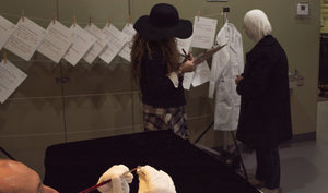 James Leonard - A woman in a floppy hat fills out a questionnaire about what she wants to Transform/Sustain, while an older woman looks at a clothesline which is pinned with others' handwritten answers to these questions